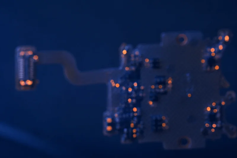 Dark blue close-up of a flex PCB assembly with copper pads and electronic components
